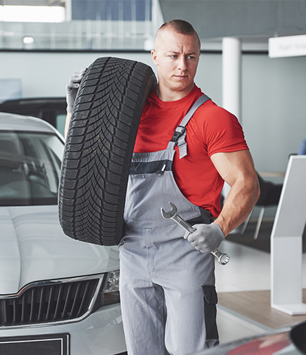 ein Mitarbeiter in Arbeitskleidung ein Auto-Rad hält